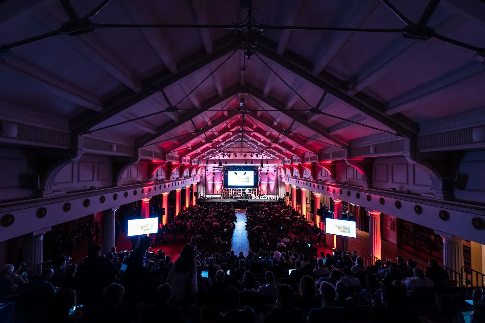Mainstage opening at SaaStock Europe 2017, RDS Industries Hall, Dublin — packed audience under the original Victorian timber-vaulted roof lit red and pink