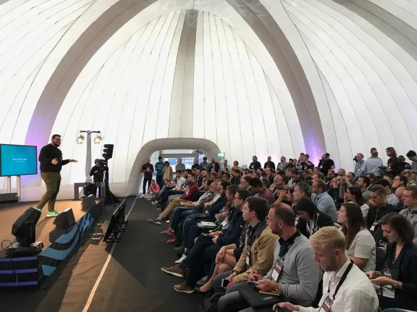 Live during SaaStock Europe 2018 — Growth Stage session inside the inflatable white-fabric dome at RDS Simmonscourt: speaker in green sneakers at stage left, an attendee with a Hygge-style coat front-row, packed seated audience under the dome's vaulted panels