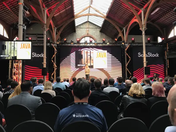 Live during SaaStock Europe 2018 — Pitch Stage in the RDS Industries Hall with a 'HOW TO PROGRAM JAVA / WHY SAAS?' slide repeated on the side screens, audience in seated rows and a front-row attendee in a TORQ INTEGRATE jacket