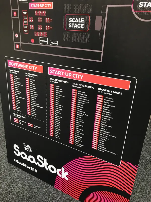 On-site signage at SaaStock Europe 2018 — bottom panel of the floor-plan board angled view: SOFTWARE CITY Gold/Silver Stands list and START-UP CITY Traction (Oct 16 / 17) + Growth Stands list, with the SaaStock '18 wave logotype and the #SaaStock18 hashtag at the bottom