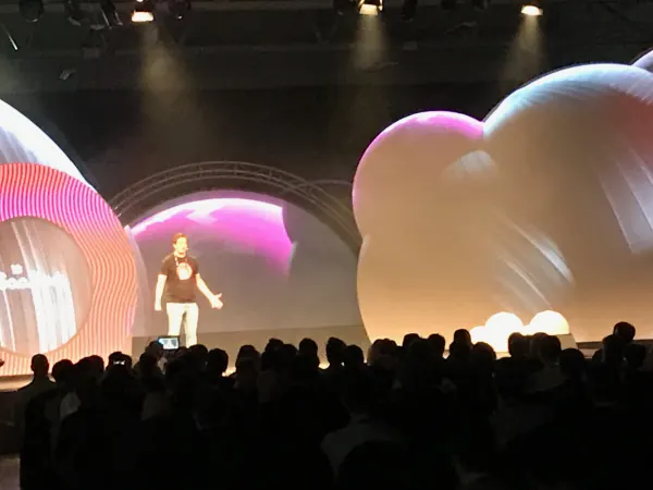 Live during SaaStock Europe 2019 — Mainstage speaker mid-talk with arms open in front of the inflatable-balloon set, packed audience silhouettes in the foreground, RDS Simmonscourt Dublin