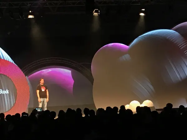 Live during SaaStock Europe 2019 — Mainstage speaker in a SaaStock tee shot from a low angle in the audience, with the ring screen and inflatable-balloon set lit behind, RDS Simmonscourt Dublin