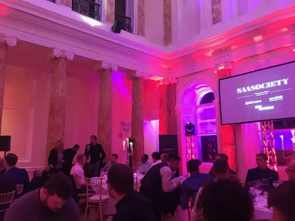 SaaSociety Founder Retreat 2019 — gala dinner at Powerscourt Hotel, founders seated under the SAASOCIETY title screen in the columned ballroom