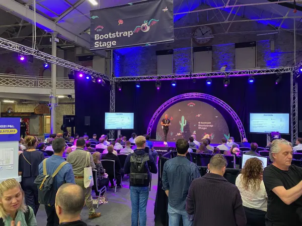Live during SaaStock Europe 2022 — wider view of the Bootstrap Stage with a presenter mid-talk and side-screen P&L slide showing 2021 numbers, packed audience and Founderpath branding visible