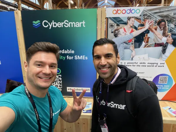 Live during SaaStock Europe 2022 — selfie at the CyberSmart sponsor booth at SaaStock Dublin 2022 with the 'Simple affordable cybersecurity for SMEs' wall and the neighbouring Abodoo skills-matching booth visible at right