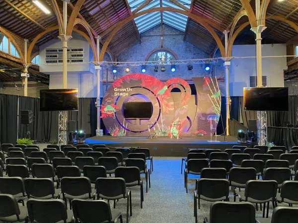 Before doors at SaaStock Europe 2022 — empty Growth Stage at the Dublin venue with the floral / red foliage LED backdrop lit, side screens showing 'OMI · Flashpoint · PSG · Capnamic · Accel' sponsor logos