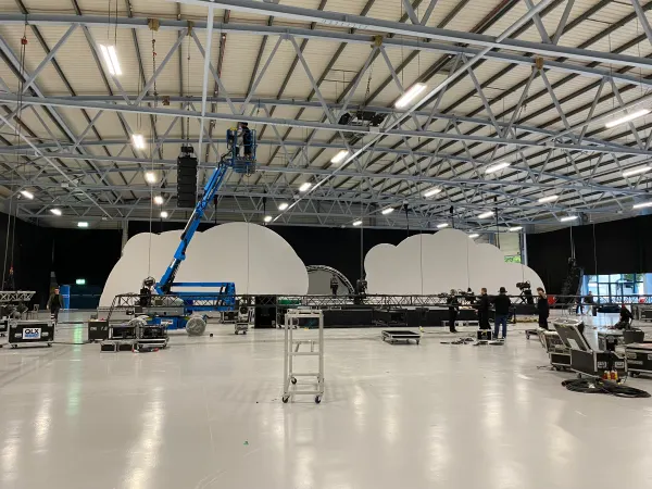 Before doors at SaaStock Europe 2022 — Mainstage build at the Dublin venue with crew on a blue cherry picker hanging gear above the cloud-shaped LED set sections, empty hall in foreground