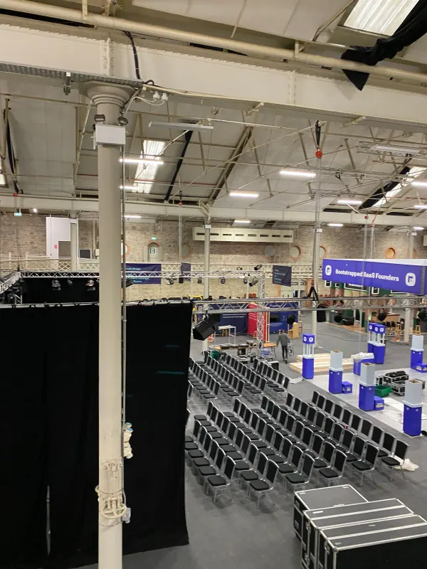 Before doors at SaaStock Europe 2022 — empty Mainstage seating area at the SaaStock Dublin venue with the 'Bootstrapped SaaS Founders' banner visible across the hall, mid-build crates still in shot