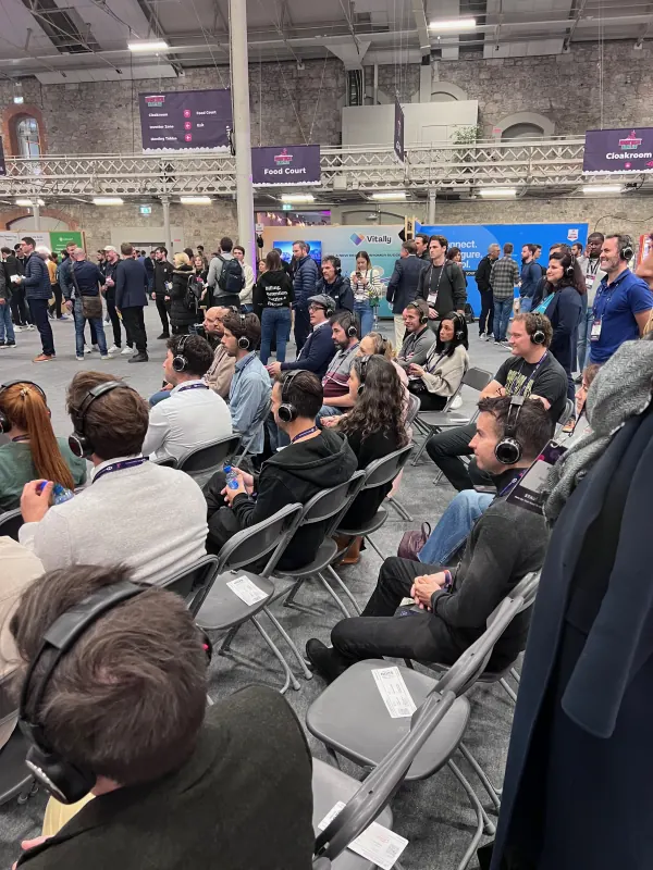 Live during SaaStock Europe 2023 — attendees watching a silent-disco-style session with branded headphones, queued up in front of the Vitally booth at RDS Simmonscourt, Dublin