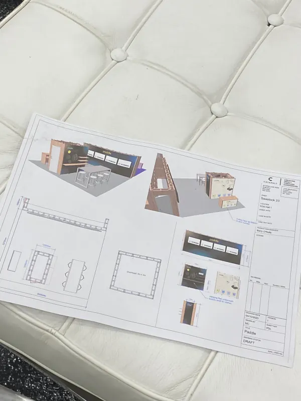 Behind the scenes at SaaStock Europe 2023 — Catapult Exhibition Sciences booth design draft for the Paddle stand at SaaStock 23, resting on a white tufted couch