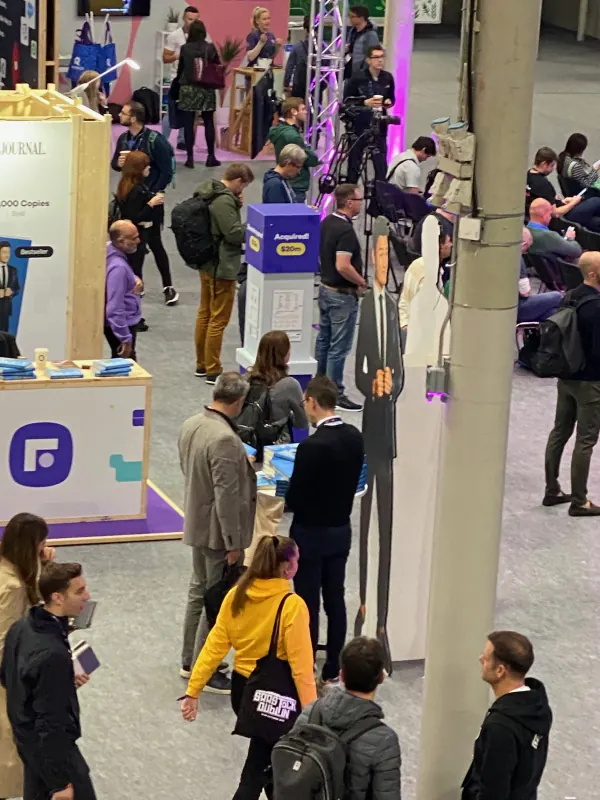 Live during SaaStock Europe 2023 — busy expo aisle at peak with attendees clustered three-deep around the Founderpath booth and an Anquiroll cardboard cut-out
