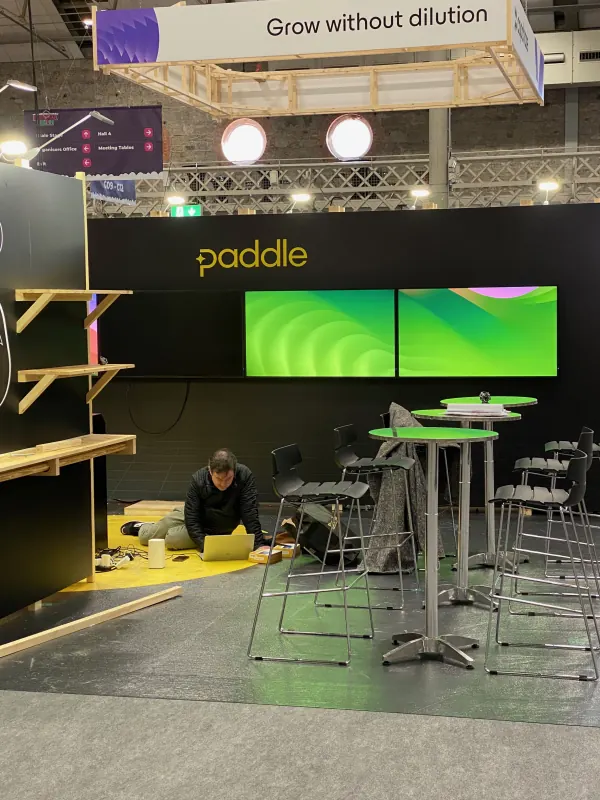 Before doors at SaaStock Europe 2023 — Paddle sponsor booth mid-setup with 'Grow without dilution' hanging banner and green-lit displays, Dublin