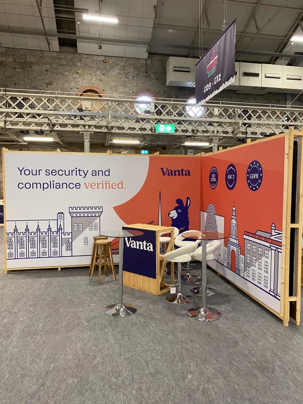 Before doors at SaaStock Europe 2023 — Vanta sponsor booth featuring 'Your security and compliance verified' wall with SOC 2 and GDPR badges and a Dublin-castle-skyline backdrop