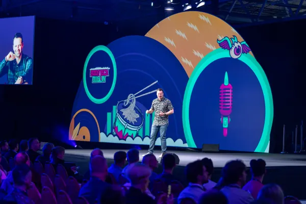 Live during SaaStock Europe 2023 — Mainstage host front-and-center on the SaaStock Dublin LED set, with a side IMAG screen showing his close-up portrait at left