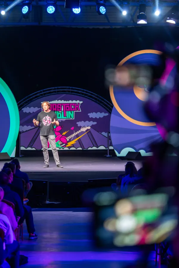 Live during SaaStock Europe 2023 — Mainstage keynote shot through the audience: a phone in the foreground filming the speaker on the SaaStock Dublin record-player set