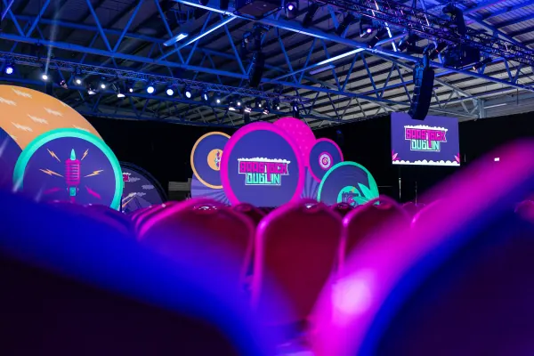 Before doors at SaaStock Europe 2023 — Mainstage seen from the rear of the auditorium, RDS Simmonscourt, with the full SaaStock Dublin LED set lit (record player, megaphone, microphone illustrations) and red velvet seat-backs in the foreground