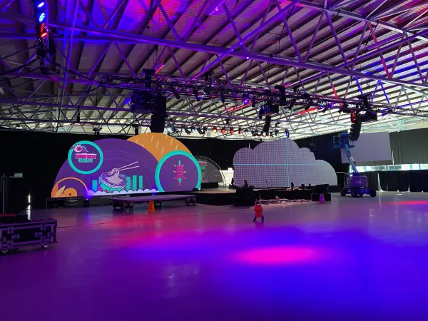 Behind the scenes at SaaStock Europe 2023 — Mainstage mid-build at RDS Simmonscourt with curved LED panels, a cloud-shaped pixel display, and overhead truss lighting in magenta and teal, Dublin