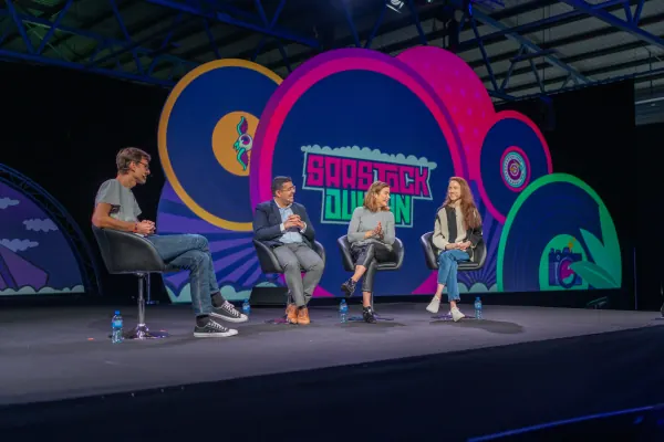 Live during SaaStock Europe 2023 — Mainstage panel of four (three men and one woman) seated on chairs across the SaaStock Dublin LED-set stage, RDS Simmonscourt