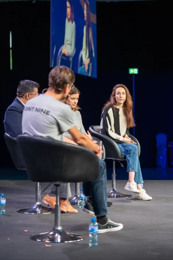 Live during SaaStock Europe 2023 — Mainstage panel of three from a side angle, the panelist on the left wearing a Point Nine VC branded tee, with the IMAG screen showing the woman speaking on the right