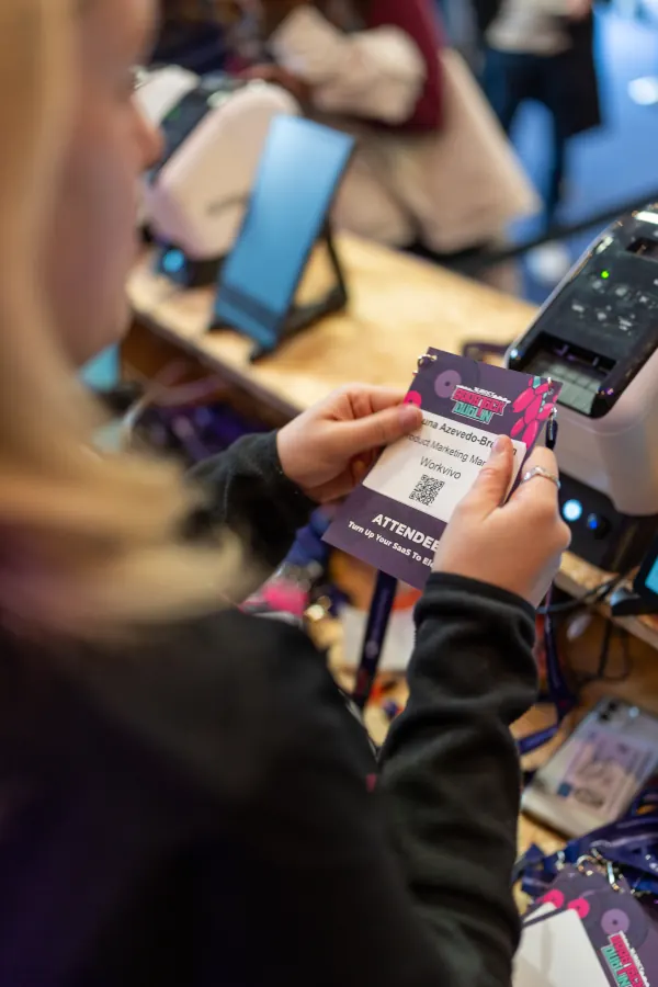 Live during SaaStock Europe 2023 — close-up of an attendee badge being printed at registration on day 1, with a thermal printer and the pink-and-purple SaaStock 2023 lanyard visible