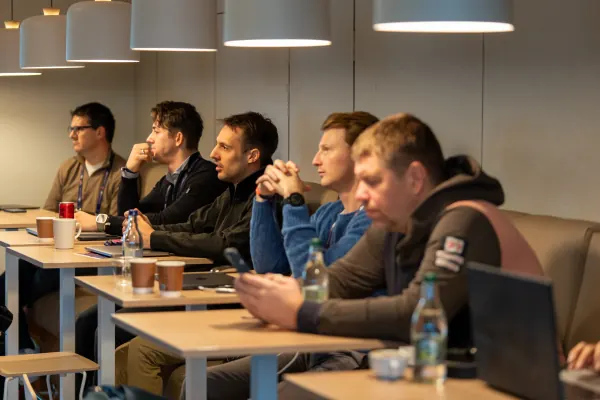 Live at SaaStock Europe 2023 Startup Day, Zendesk Dublin — five attendees in a row at a long table side-on, all listening, under the Zendesk office's pendant lighting