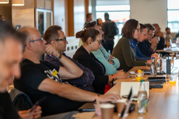 Live at SaaStock Europe 2023 Startup Day, Zendesk Dublin — a row of attentive attendees seated at a long table, all with SaaStock 2023 lanyards, mid-session