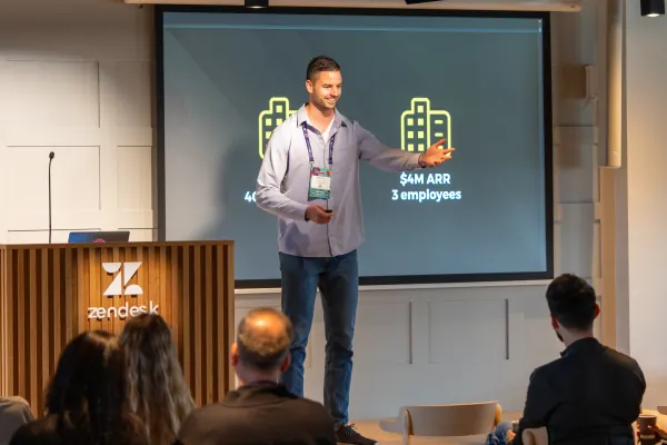 Live at SaaStock Europe 2023 Startup Day, Zendesk Dublin — Founderpath founder Nathan Latka on stage in a grey shirt holding a remote, with '$4M ARR · 3 employees' on the slide behind him, beside the Zendesk-branded podium