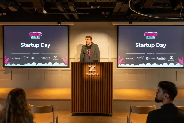 Live at SaaStock Europe 2023 Startup Day — speaker behind the Zendesk-branded podium with twin 'Startup Day' slides on both sides showing AppSumo, CMS Hub, Intercom, SaaStock and Zendesk sponsor logos