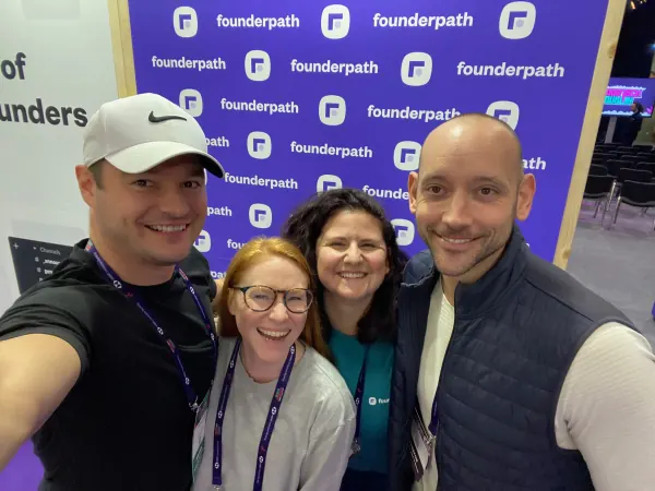 Live during SaaStock Europe 2023 — four members of the Founderpath team smiling for a selfie in front of the Founderpath logo step-and-repeat at the Dublin expo