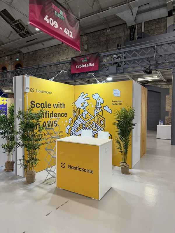 Before doors at SaaStock Europe 2025 — ElasticScale yellow booth with 'Scale with confidence on AWS' messaging, booth numbers 409–412, Tabletalks signage above