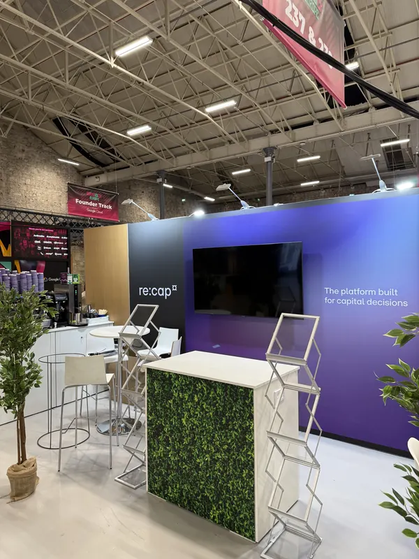 Before doors at SaaStock Europe 2025 — re:cap purple booth with 'The platform built for capital decisions' tagline and brochure stands, faux-hedge meeting counter
