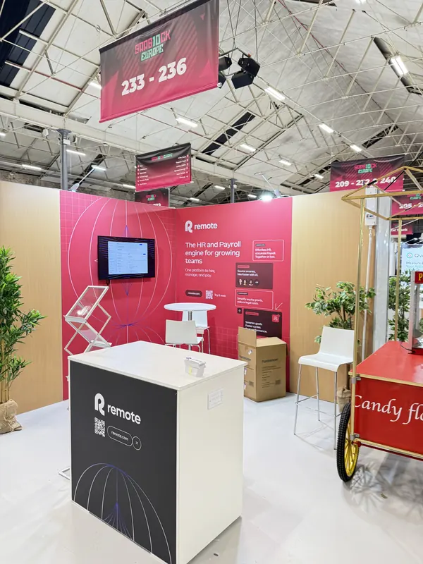 Before doors at SaaStock Europe 2025 — Remote booth at 233–236 with 'The HR and Payroll engine for growing teams' messaging and brochure stands, candy-floss cart visible beside