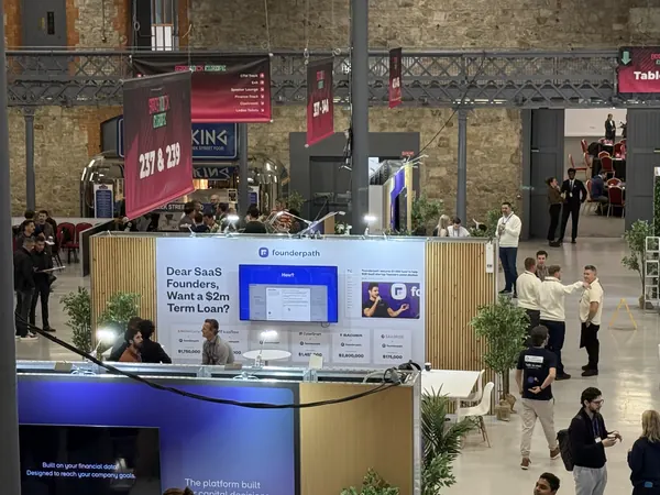 Live during SaaStock Europe 2025 — second balcony view of the Founderpath booth showing the meeting-area side of the stand with attendees seated in conversation