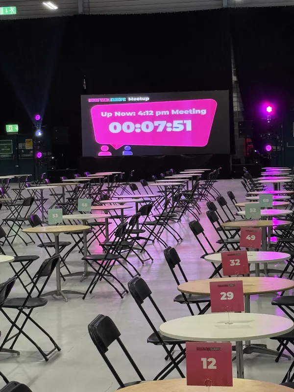 Behind the scenes at SaaStock Europe 2025 — empty 1:1 meeting floor with the live meeting-countdown screen above showing 'Up next 4:02 pm meeting — 00:07:51'