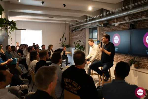 Live at SaaStock Local Amsterdam Q2 2024 — alternate wide-angle of the room mid-talk, audience packed in, panelists at the front-right