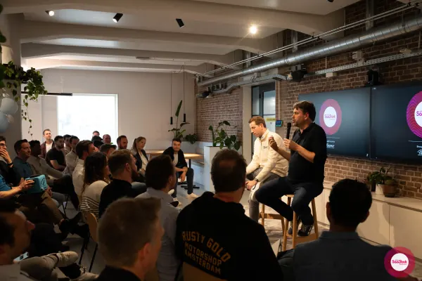 Live at SaaStock Local Amsterdam Q2 2024 — wide view from the back of the room showing the full seated audience with a 'Rusty Gold Motorshop Amsterdam' hoodie in the foreground and panelists in the distance