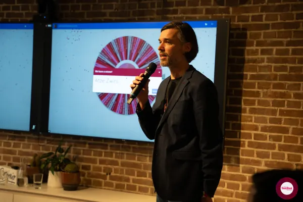 Ferdinand Goetzen at the mic next to a wheel landing on 'We have a winner! Atze Zwirs' at SaaStock Local Amsterdam Q2 2024