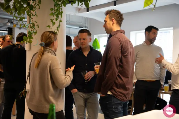 Live at SaaStock Local Amsterdam Q2 2024 — a trio of founders in conversation with drinks in hand at Personio's Amsterdam office, hanging plants overhead
