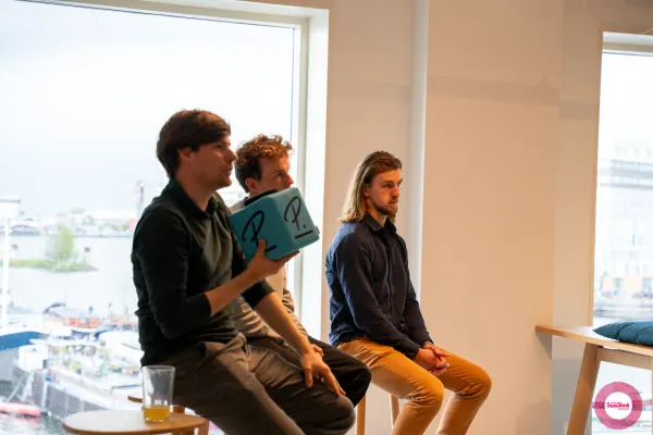 Live at SaaStock Local Amsterdam Q2 2024 — three panelists seated on a low bench by Personio's canal-side window, with Amsterdam waterway visible behind them, one holding a Personio P. cube