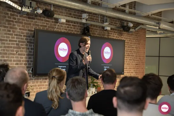 Live at SaaStock Local Amsterdam Q2 2024 — animated shot of Ferdinand Goetzen mid-sentence, microphone raised, in front of the SaaStock Local Amsterdam screens
