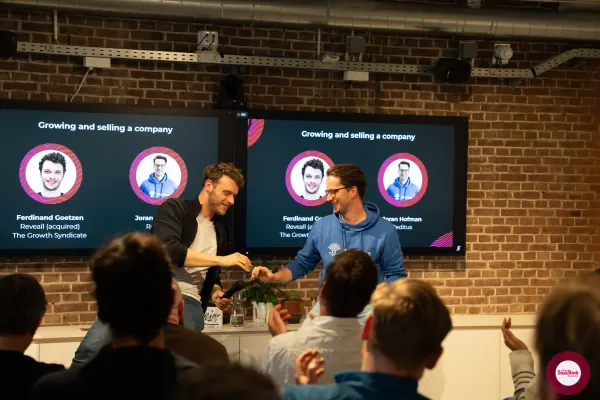 Live at SaaStock Local Amsterdam Q2 2024 — wider view of the Ferdinand and Joran handshake with the 'Growing and selling a company' slide on both screens behind them