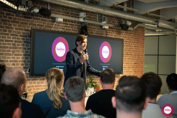 Live at SaaStock Local Amsterdam Q2 2024 — wide stage shot of Ferdinand Goetzen presenting with the SaaStock Local Amsterdam × Personio screens behind and the back of the audience in the foreground