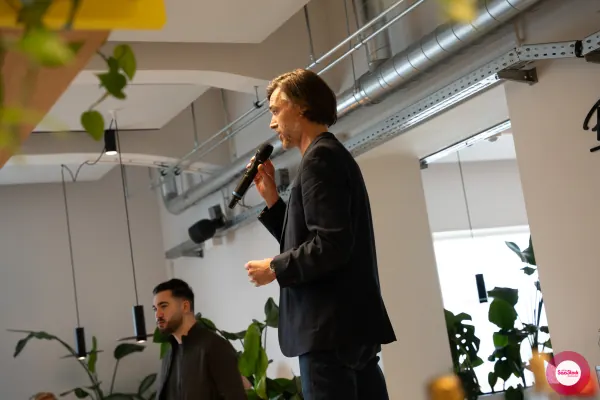 Live at SaaStock Local Amsterdam Q2 2024 — Ferdinand Goetzen mid-talk in profile, microphone in hand, against the exposed industrial ducting of Personio's Amsterdam office