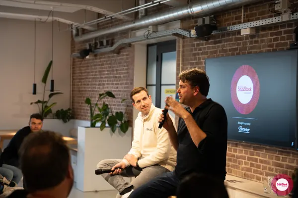 Live at SaaStock Local Amsterdam Q2 2024 — Koen Stam of Personio mid-answer on stage, gesturing with one hand while holding the microphone, the Lepaya co-founder seated alongside
