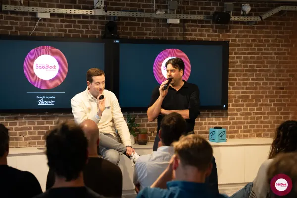 Live at SaaStock Local Amsterdam Q2 2024 — wide framing of Koen Stam (Personio) and the Lepaya co-founder seated on stage with a Personio-branded P. cube visible in front of an audience member