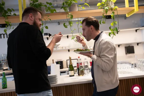 Live at SaaStock Local Amsterdam Q2 2024 — two attendees in casual sweaters eating salad plates standing at the bar at Personio's Amsterdam office