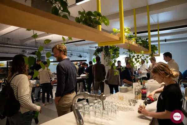Live at SaaStock Local Amsterdam Q2 2024 — view across Personio's bar showing the beer tap, lined-up wine and water glasses, and attendees gathered behind