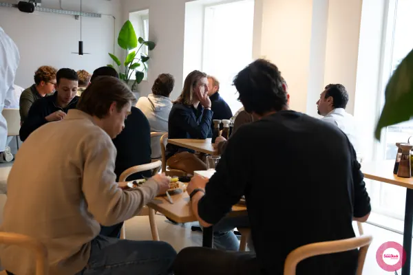 Live at SaaStock Local Amsterdam Q2 2024 — attendees seated at the white-oak tables in Personio's Amsterdam office canteen, eating and talking before the program