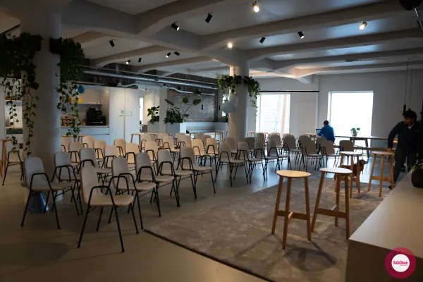 Before doors at SaaStock Local Amsterdam Q2 2024 — Personio's Amsterdam event floor with rows of empty chairs facing the front, before attendees arrived. Cream chairs, exposed brick, hanging plants