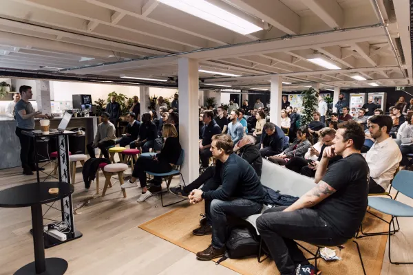 Live at SaaStock Local London — wide view of the full UK SaaS founder audience seated across the warehouse-style venue with a speaker at the podium